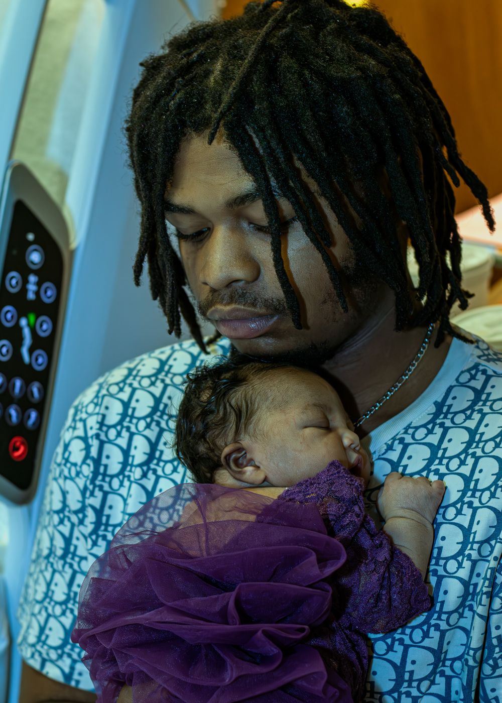 A parent in a patterned hospital gown holding a newborn baby wrapped in purple fabric.