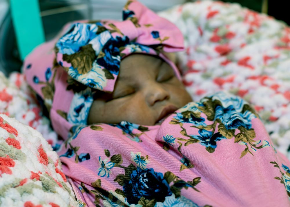 Close-up view of a sleeping baby wearing a floral headband against pink bedding.