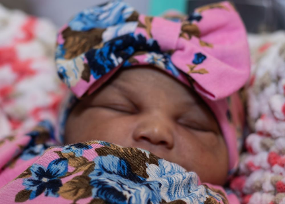 Baby resting peacefully on pink bedding with floral headband.