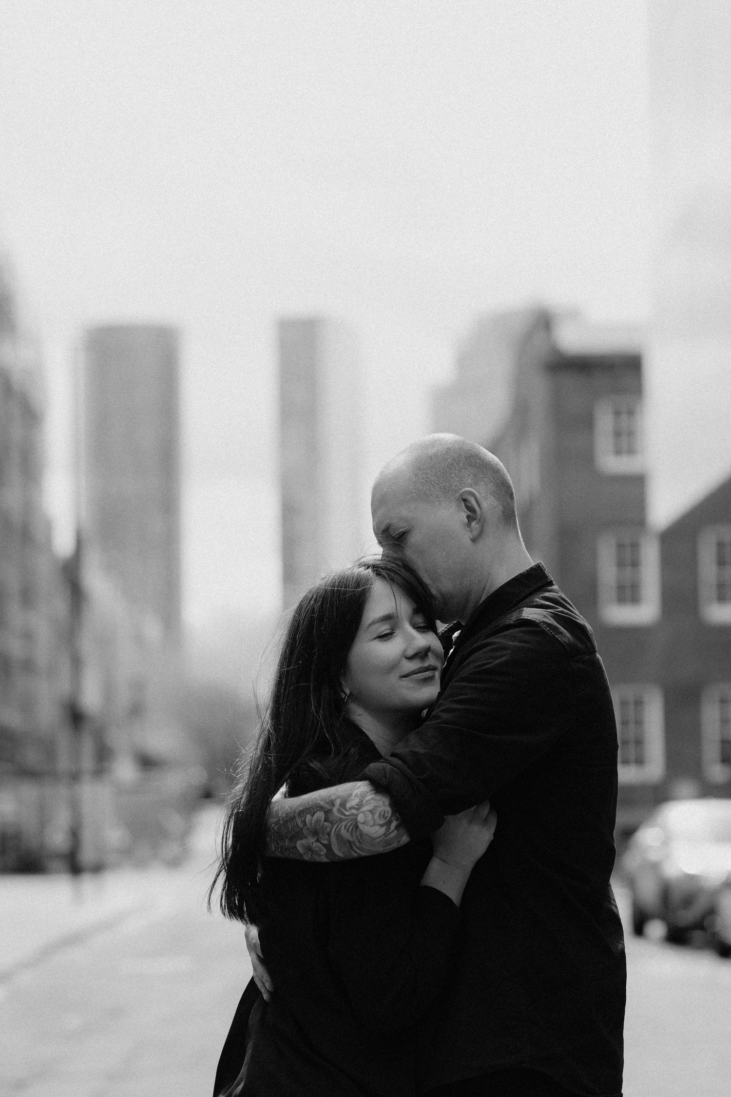 Black and white photo series of a romantic couple sharing tender moments in an urban setting with city buildings behind them.