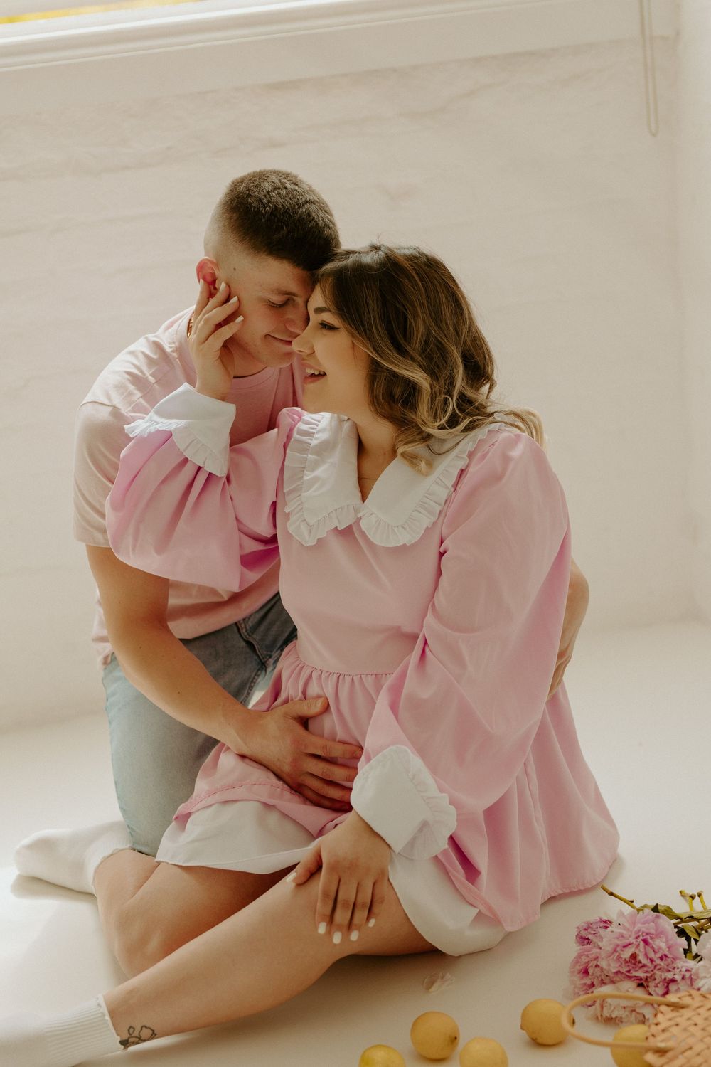A romantic couple in pink and white outfits share intimate moments in a bright, minimalist setting.