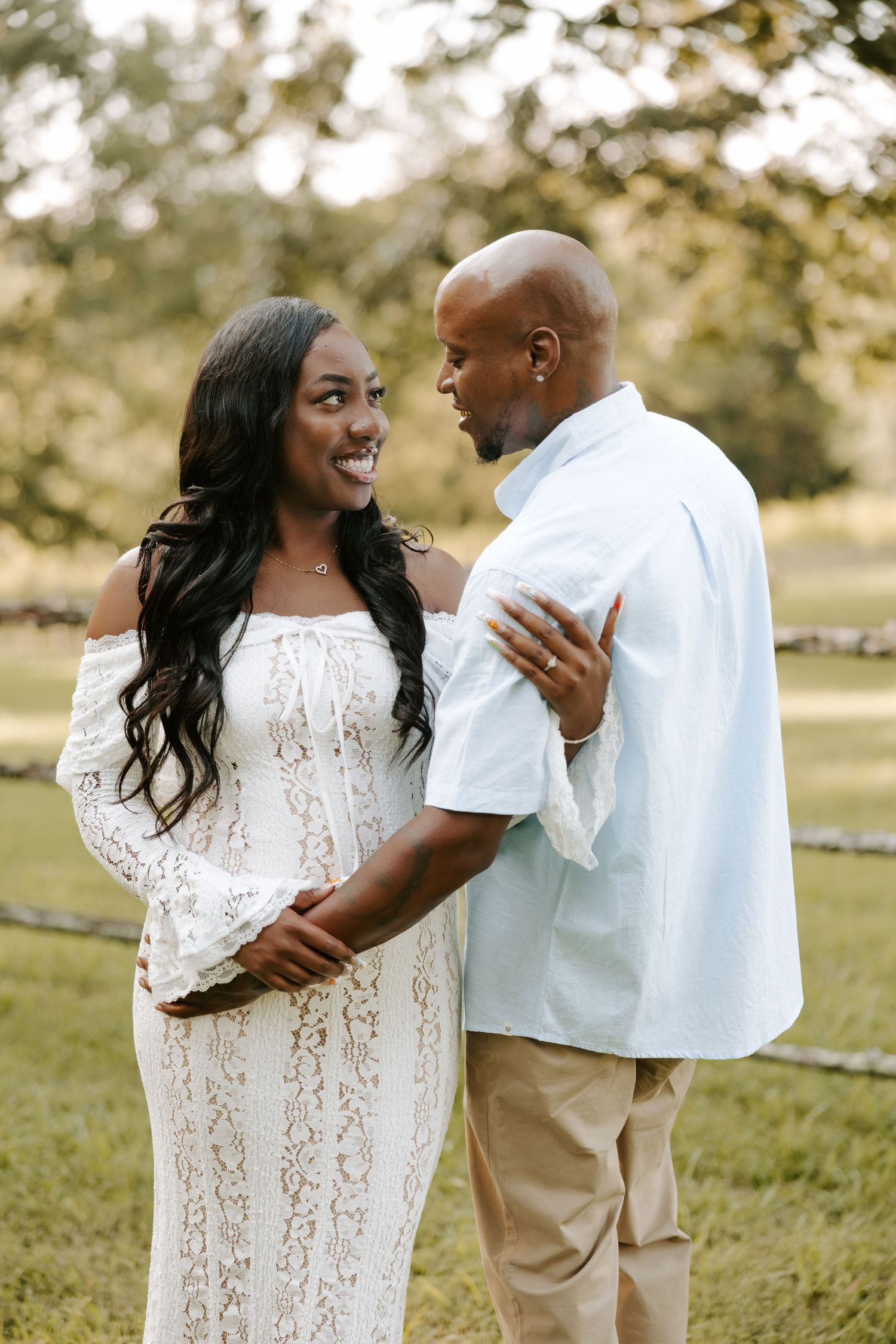 Couple in white outfits share tender moment during maternity photoshoot in grassy field.