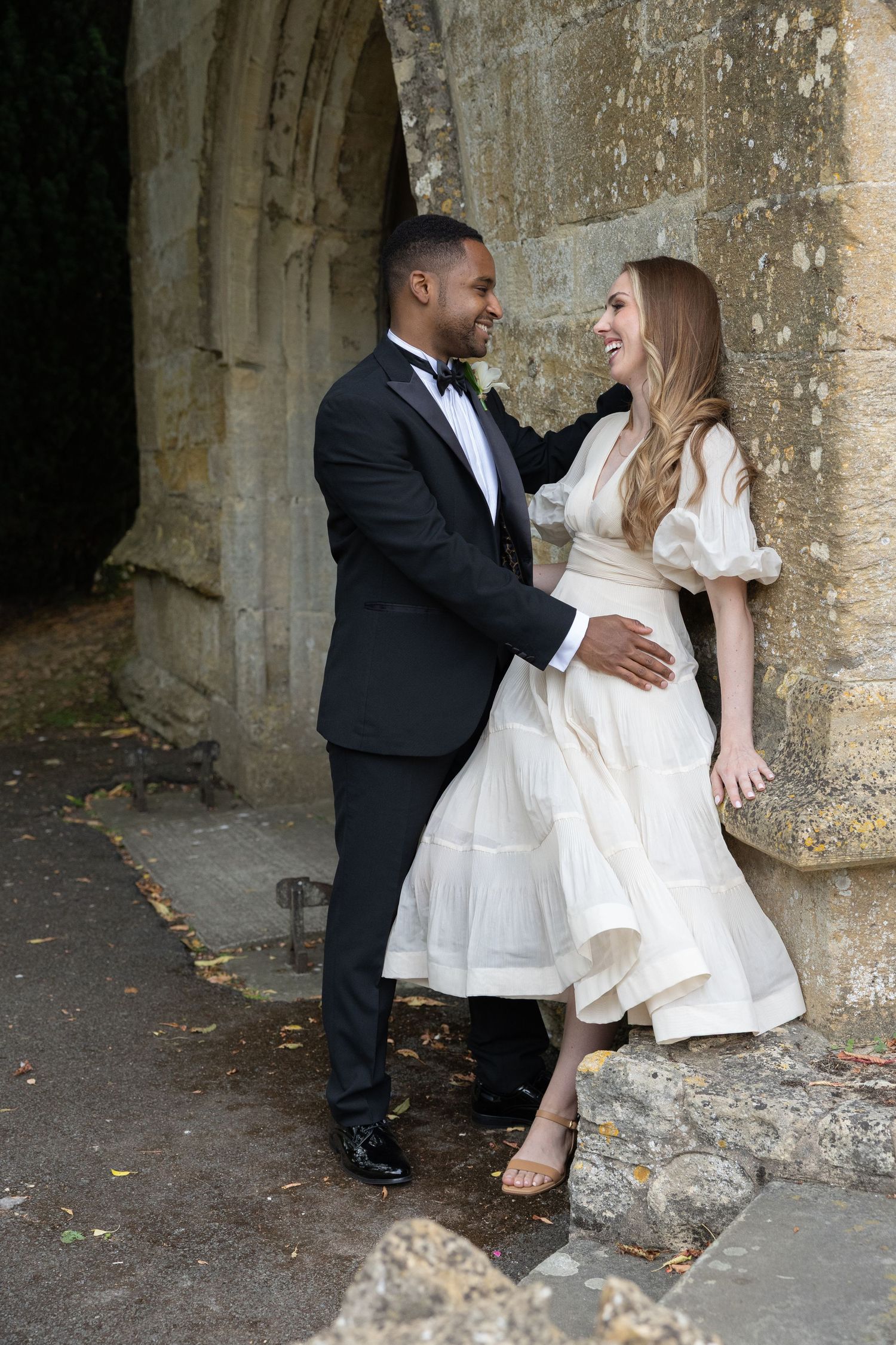 A couple in formal wedding attire shares romantic moments against a stone archway in a series of candid shots.