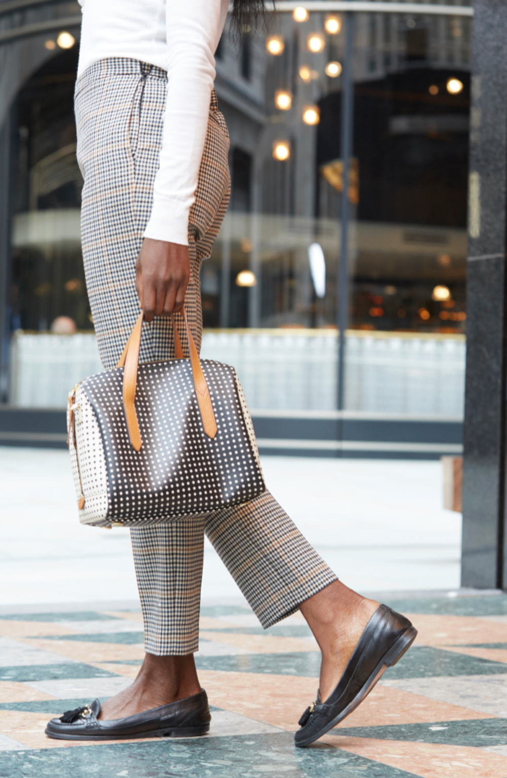 Close-up of legs wearing plaid pants and black loafers walking on urban pavement.