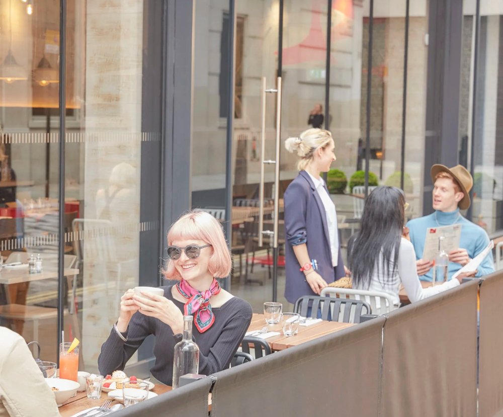 Outdoor cafe scene with customers seated at tables along modern building exterior.