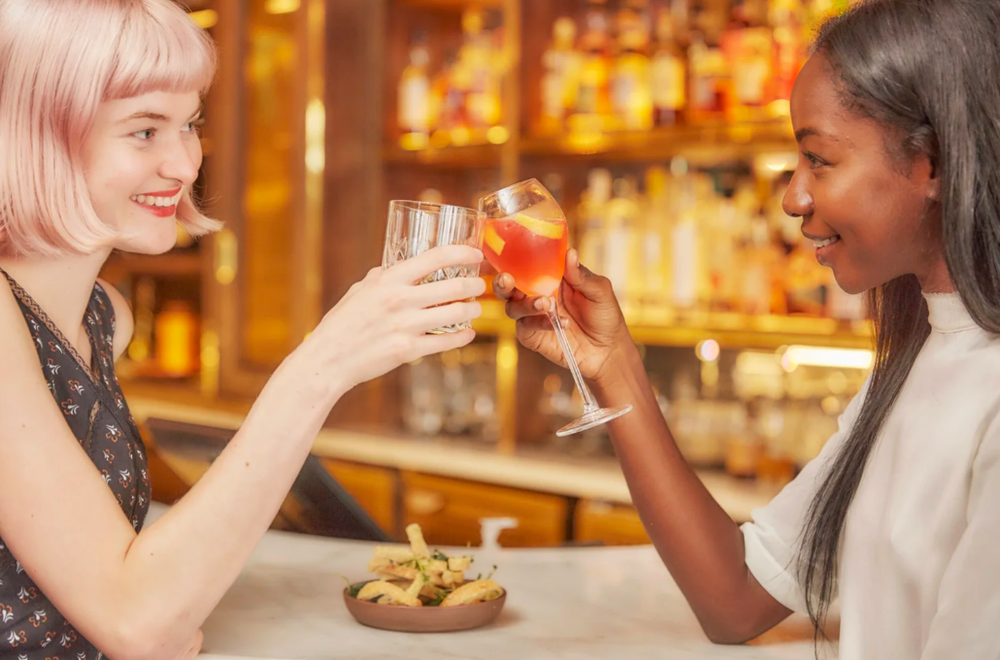 Friends enjoying drinks and conversation at a warmly lit bar or restaurant.
