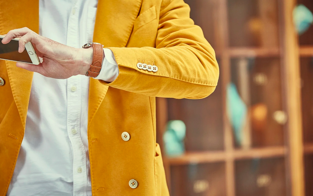 Person in yellow blazer gesturing while holding drink at social gathering.