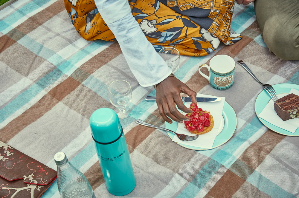 People enjoying a casual outdoor meal with plates and drinks on a checkered tablecloth.