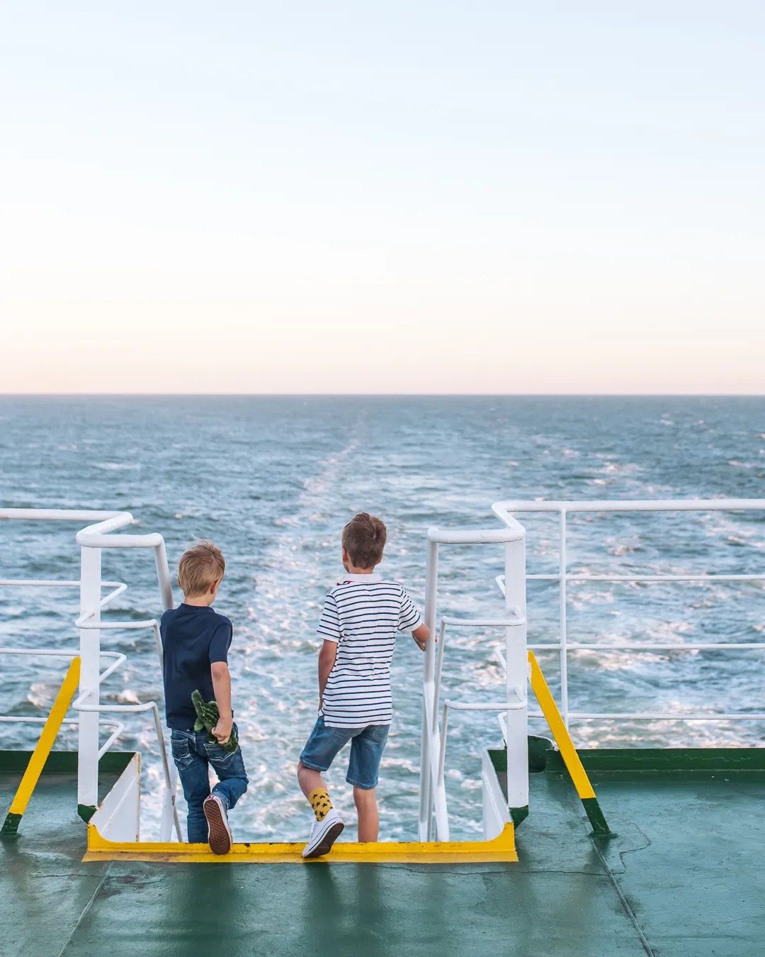 Two children standing at a ferry railing looking out at the open sea.