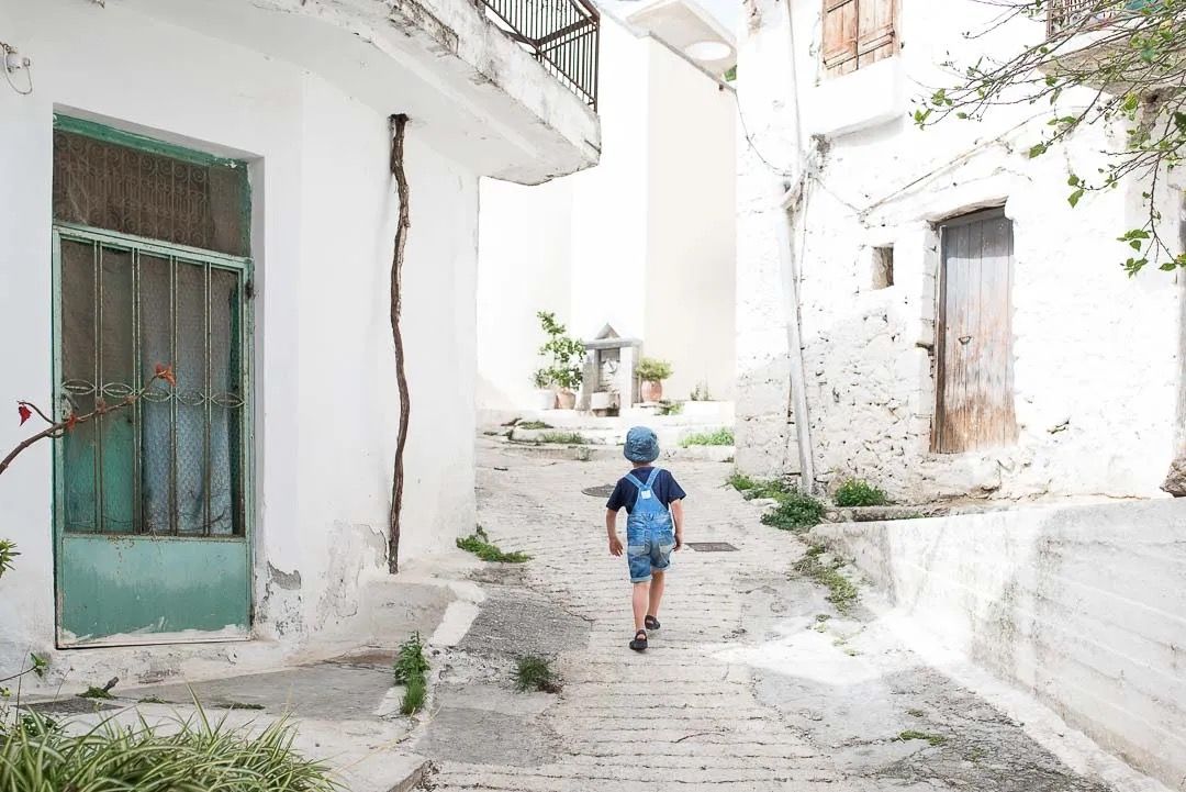 Narrow whitewashed alley with steps leading upwards between traditional Mediterranean buildings in a hillside town.
