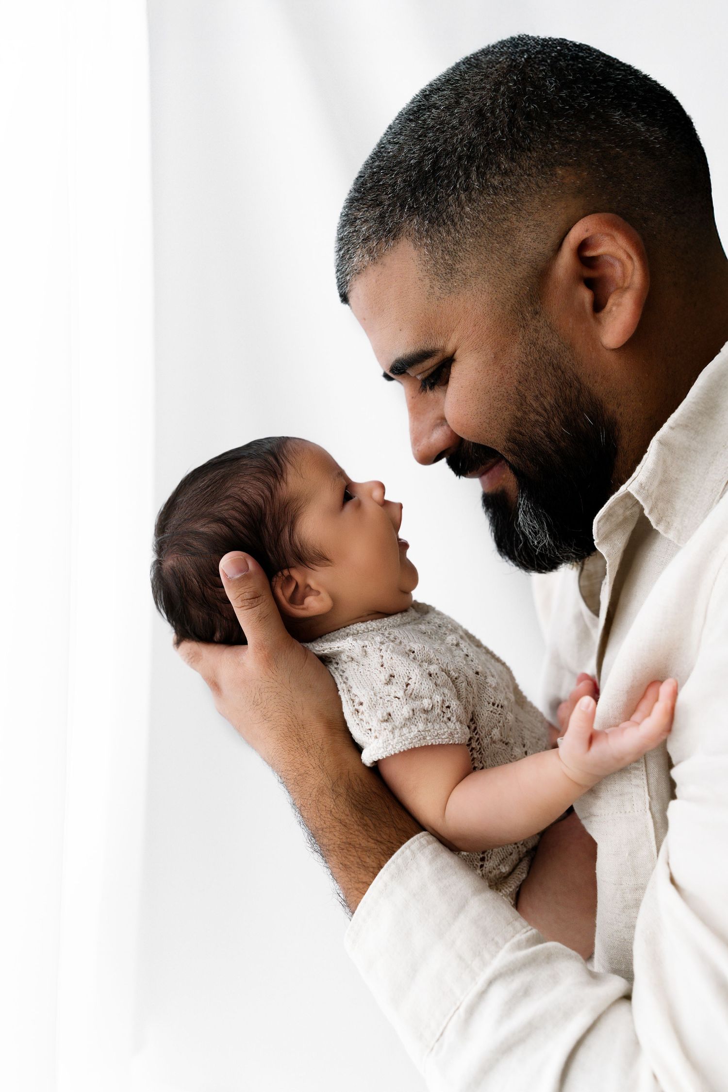 A tender moment captured in a series of photos showing a sibling gently kissing a baby in white lace clothing.