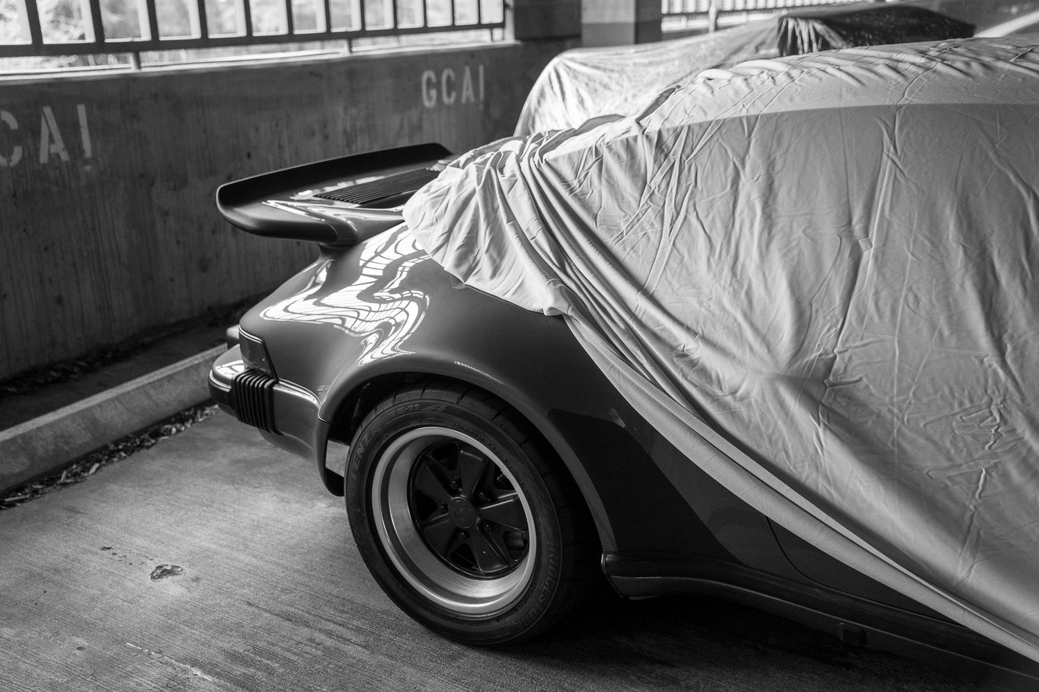 Car covers protect a row of parked vehicles from weather and debris in an outdoor storage area.