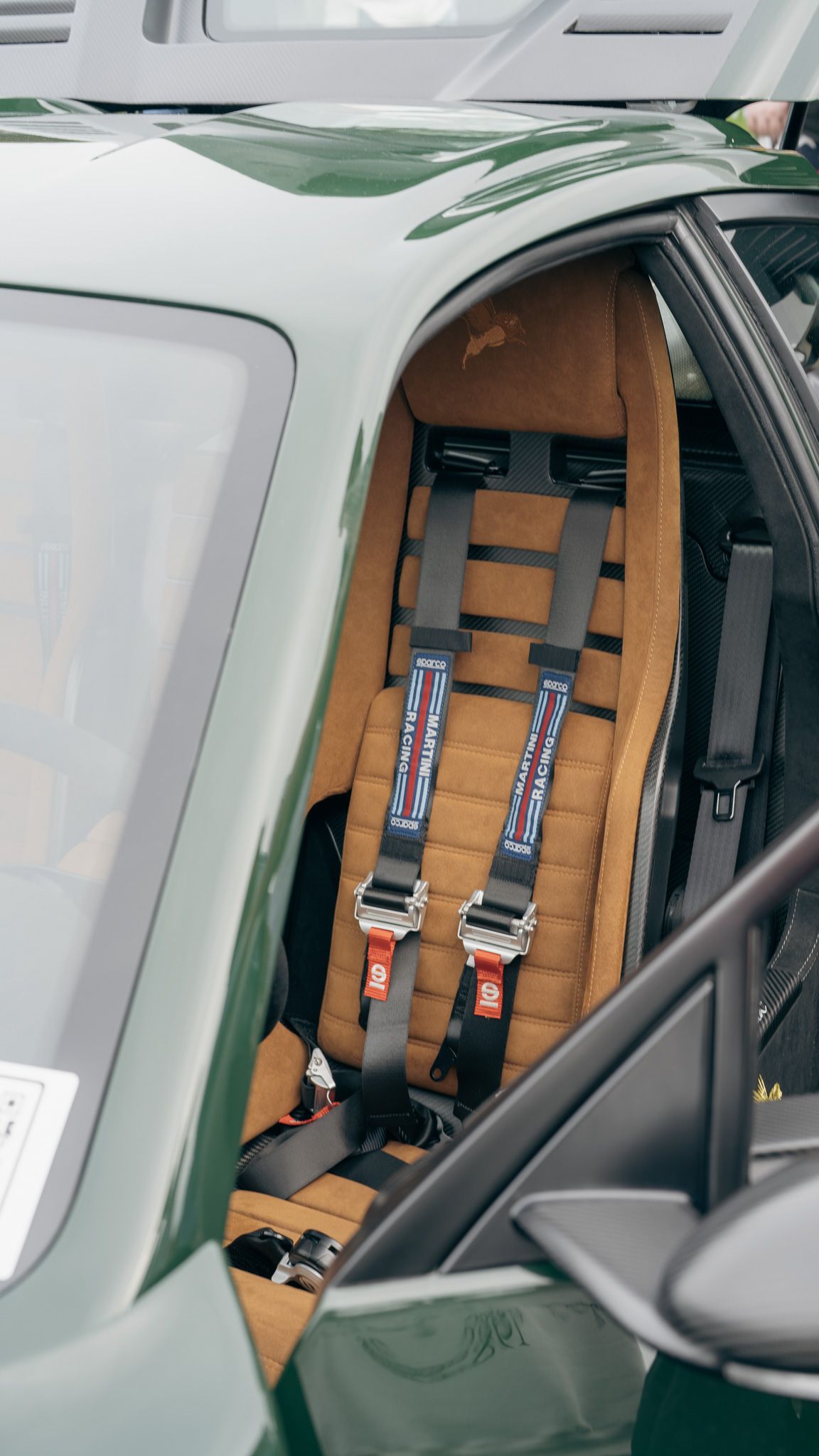 Interior view of a Ferrari F40 showing tan racing seats with Simpson safety harnesses mounted in the cockpit.