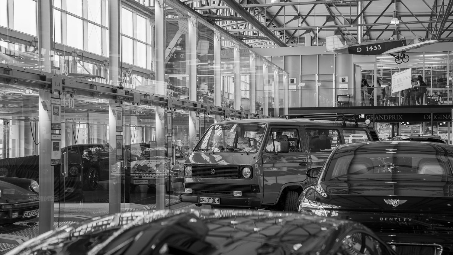 Black and white panoramic view of a vintage car showroom interior with multiple classic automobiles on display.
