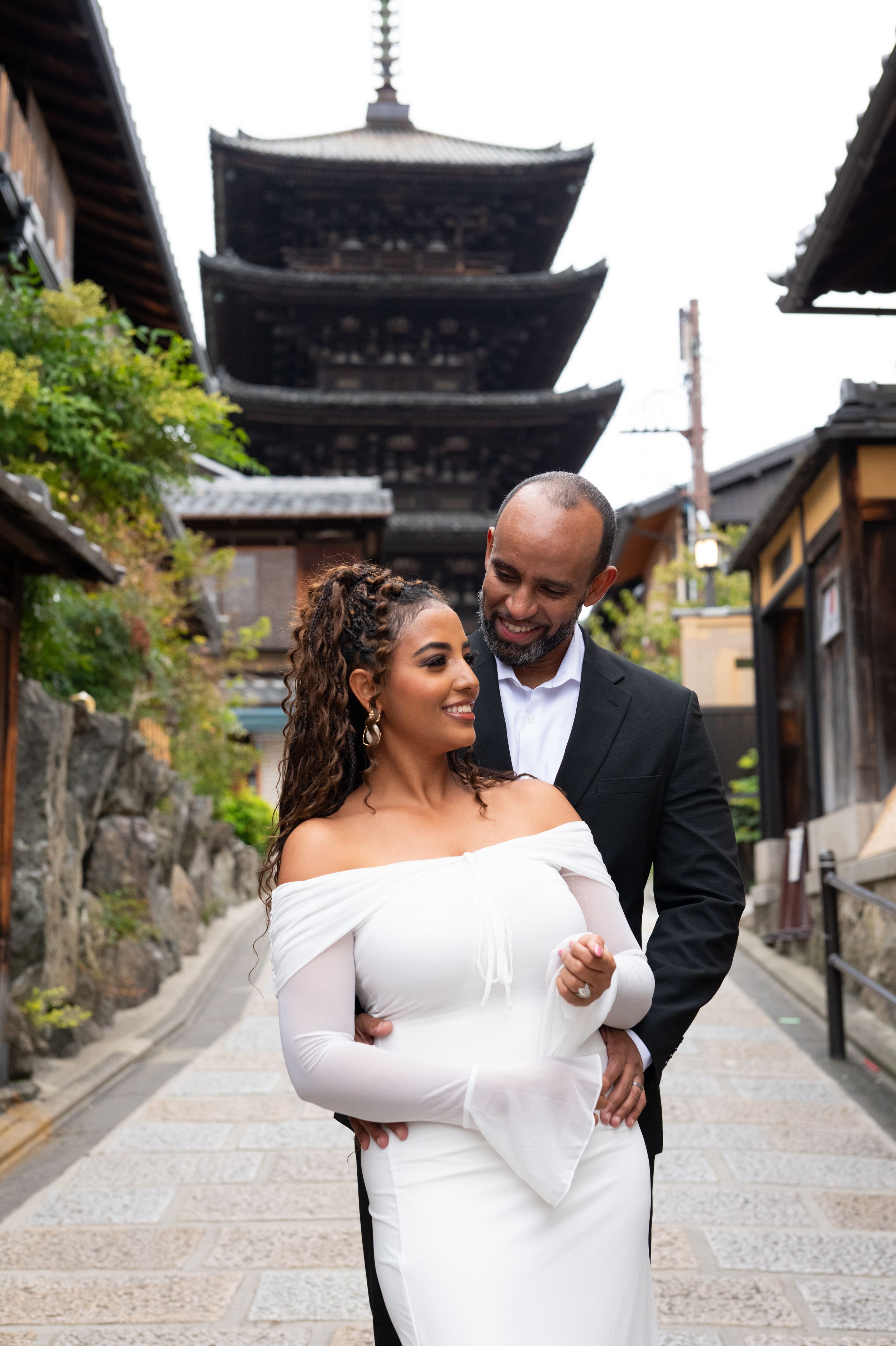 Couple posing in front of a traditional Japanese pagoda, woman in white off-shoulder gown.