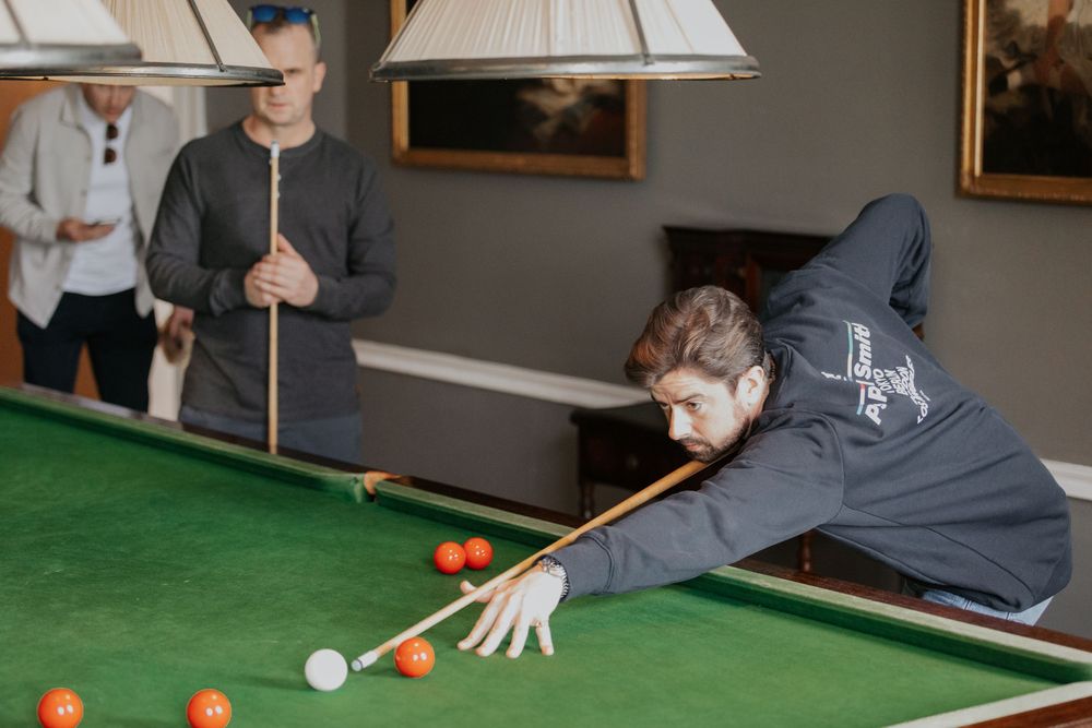 A young man leaning over a snooker table taking a shot while another player watches.