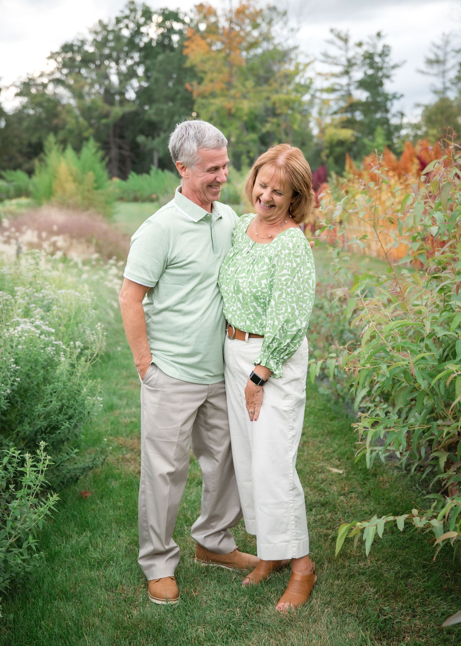 A couple in coordinating green and white outfits share a romantic moment while walking through a lush garden setting.