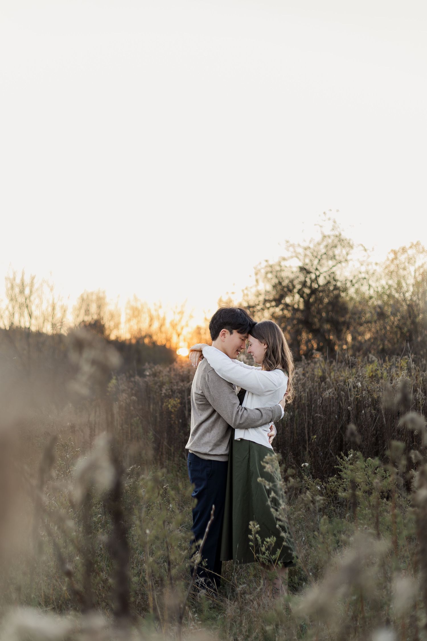 A couple shares a romantic embrace in a golden-lit meadow at sunset.