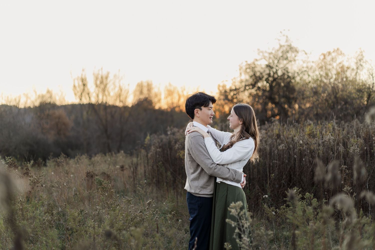 Romantic couple embraces in a golden field at sunset during a tender outdoor photo session.