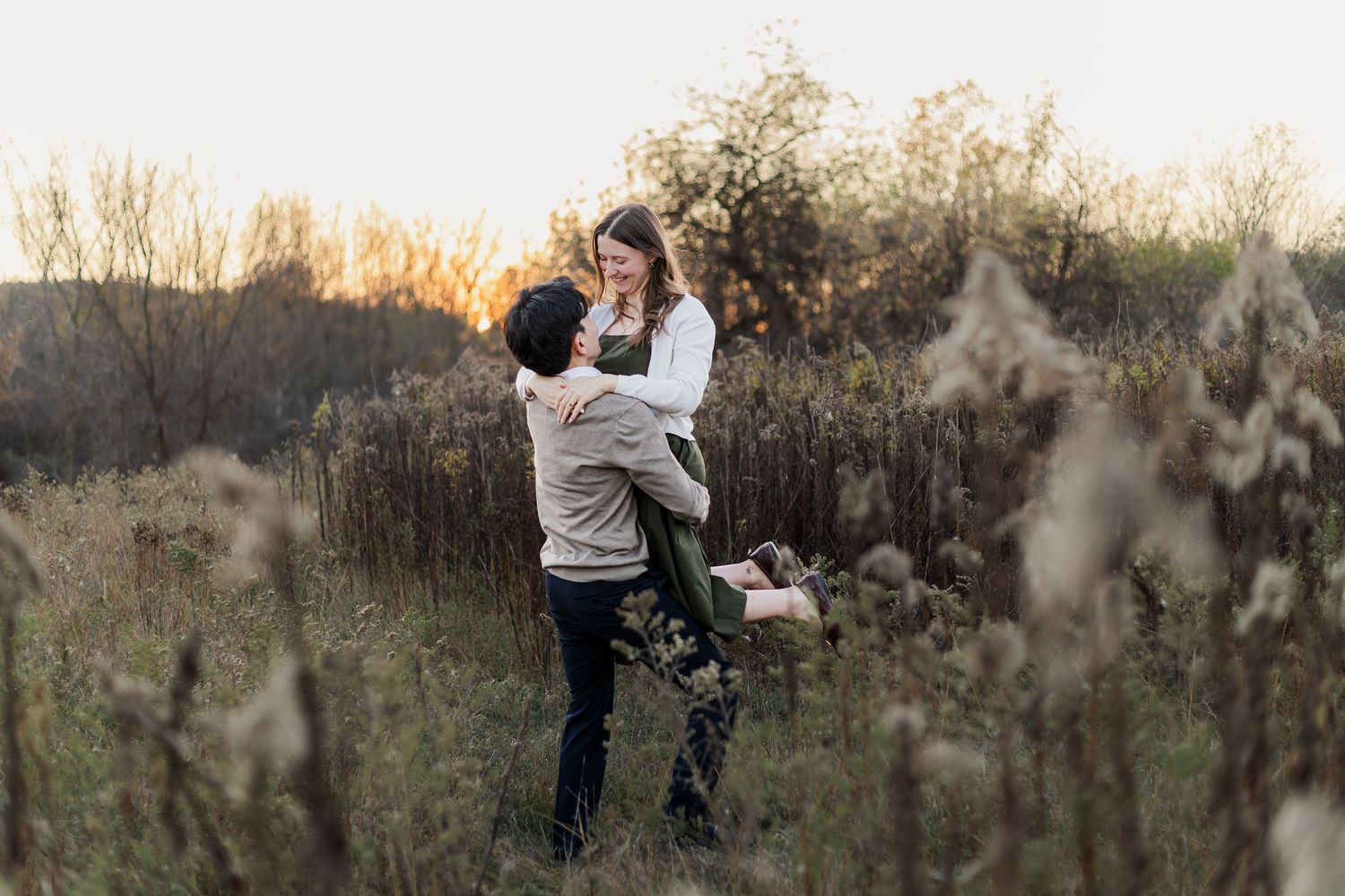 Couple shares intimate moment while dancing together in tall grass during golden hour.