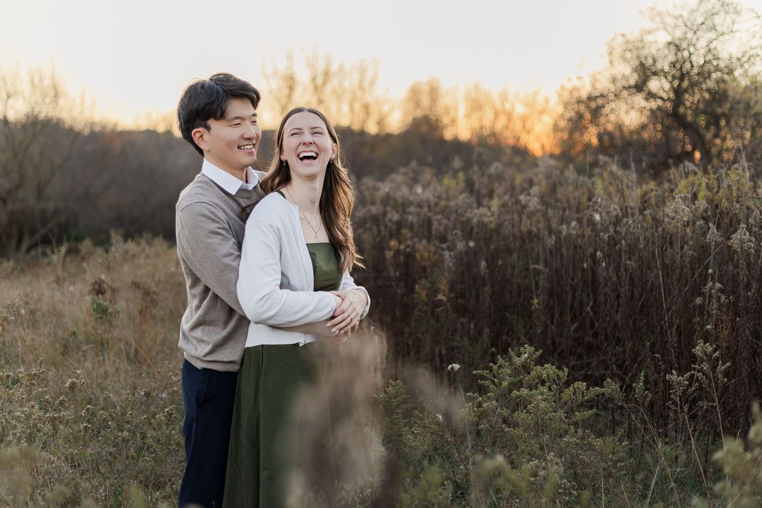 Couple dances and laughs together in a rustic field with warm autumn light filtering through.