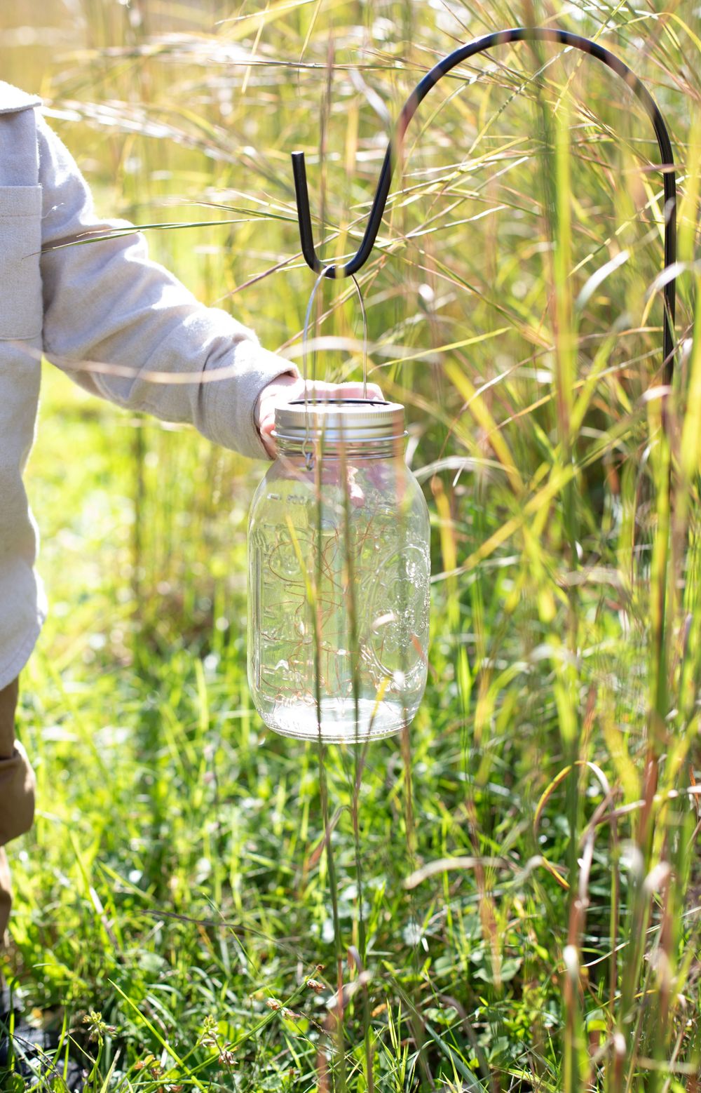 Glass mason jars sit nestled in tall grass and wildflowers on a sunny summer day.