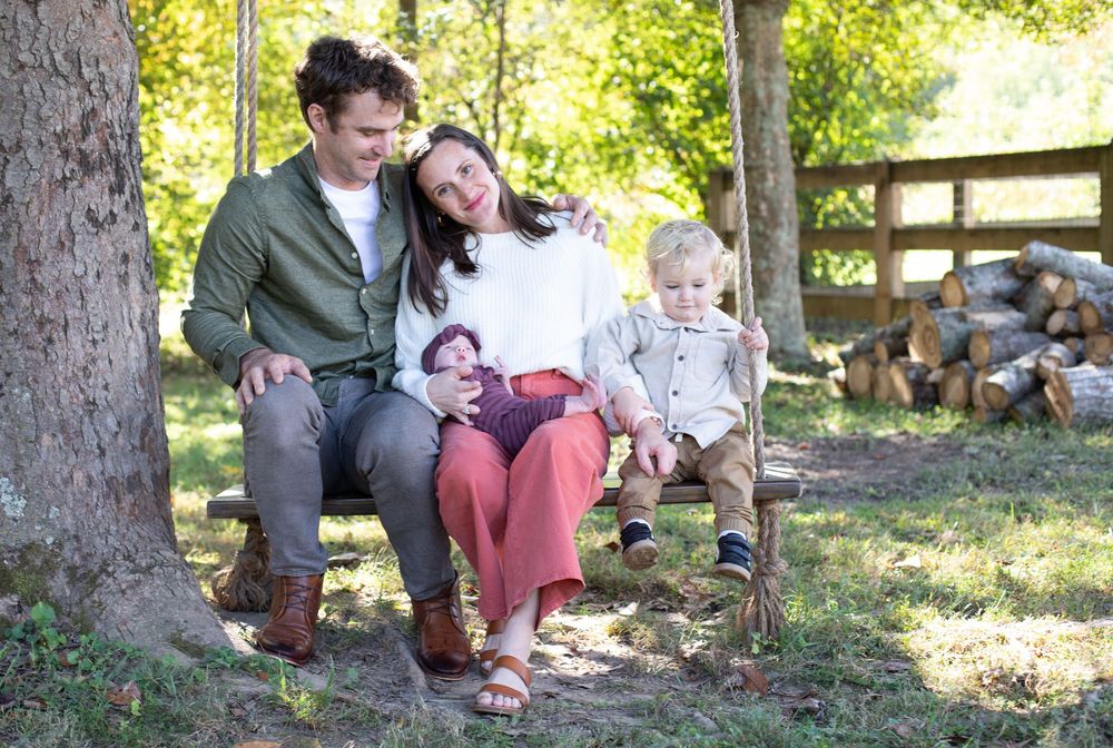 A group enjoys a picnic gathering in a wooded outdoor setting during a sunny afternoon.