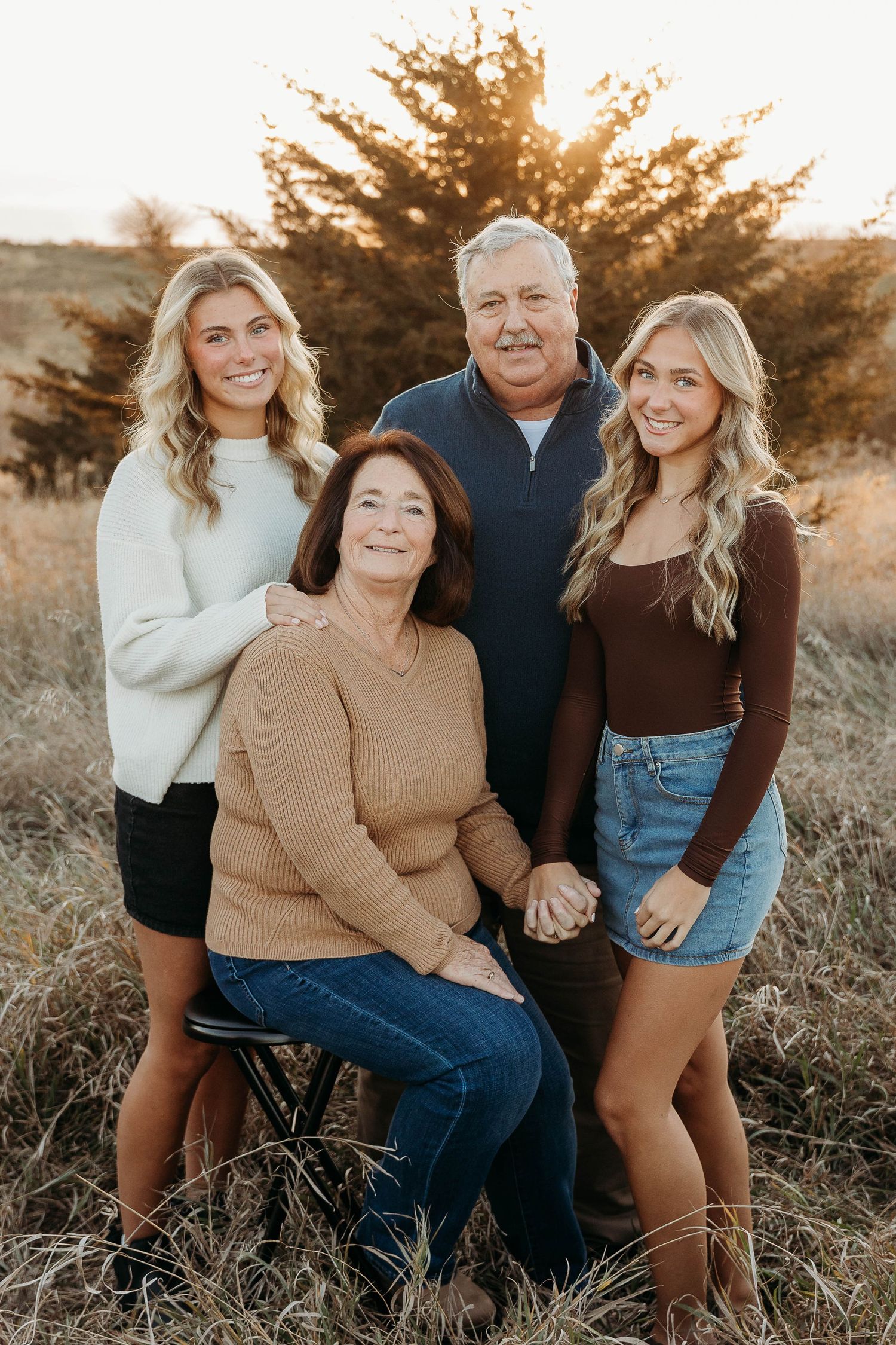 Family poses together in a grassy field during golden hour sunset in casual autumn outfits.