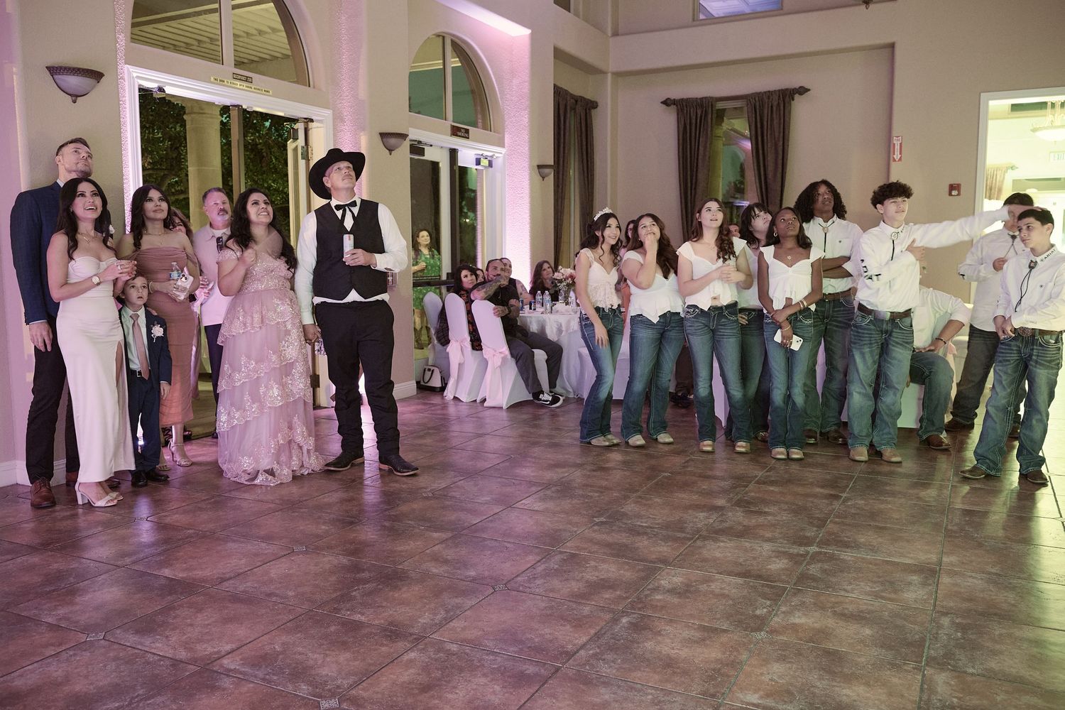 Wedding guests line the dance floor in formal attire as they watch a traditional dance performance at an elegant reception.
