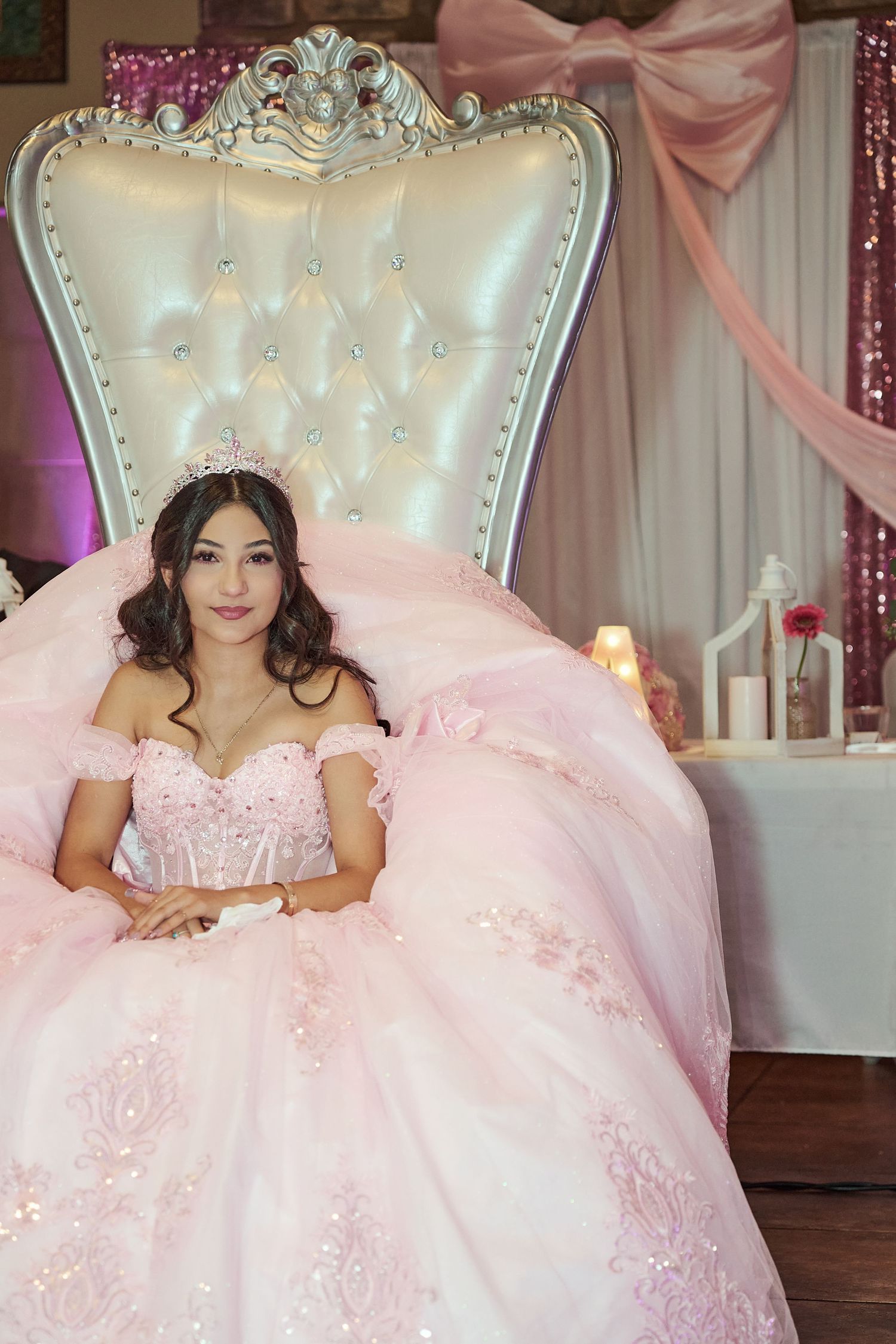 A pink tulle quinceañera dress adorned with delicate lace details sits elegantly on an ornate white throne chair.