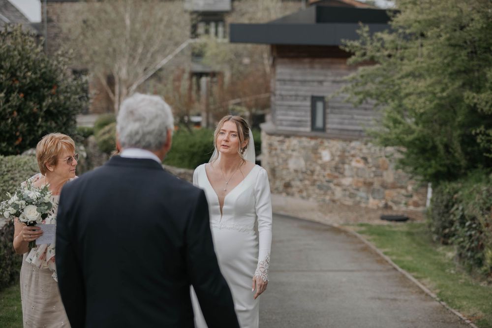 Bride in elegant white fitted gown greeting guests on a garden pathway at her wedding ceremony.