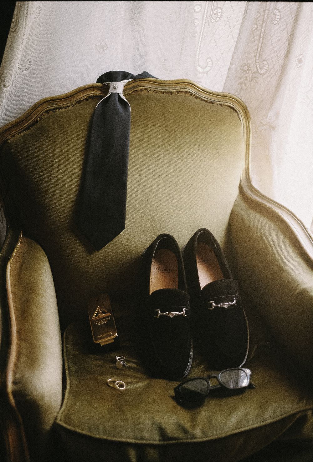 Black formal shoes and accessories arranged on a vintage beige sofa.
