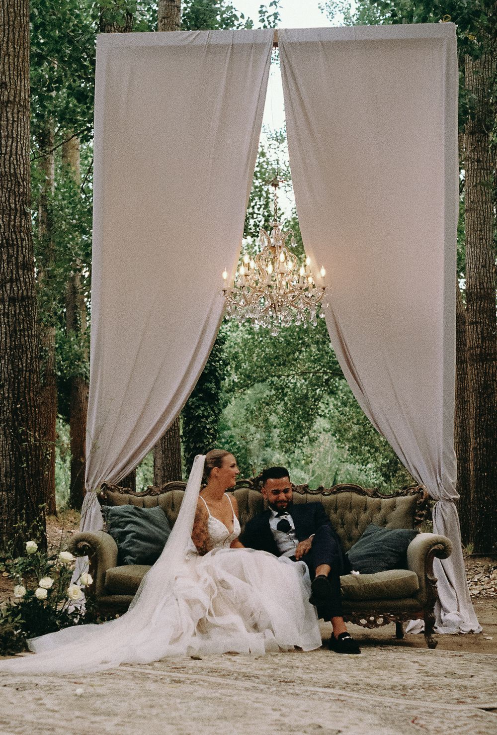Wedding scene with white draped canopy and elegant seating area in a forest setting.