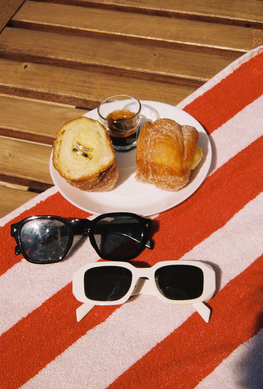 Sunglasses and pastries arranged on a red and white striped surface in natural lighting.