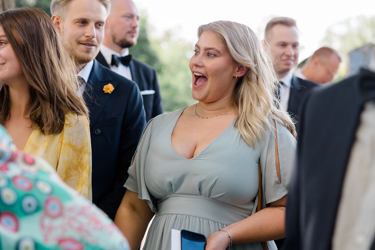 A group of people gather outdoors at a casual event, sharing laughter and conversation in natural lighting.