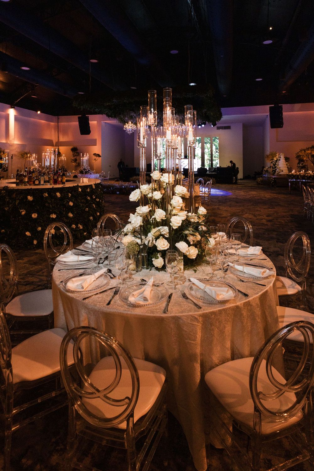 Elegant wedding reception tables with crystal chandeliers, white linens, and floral centerpieces in a dimly lit venue.