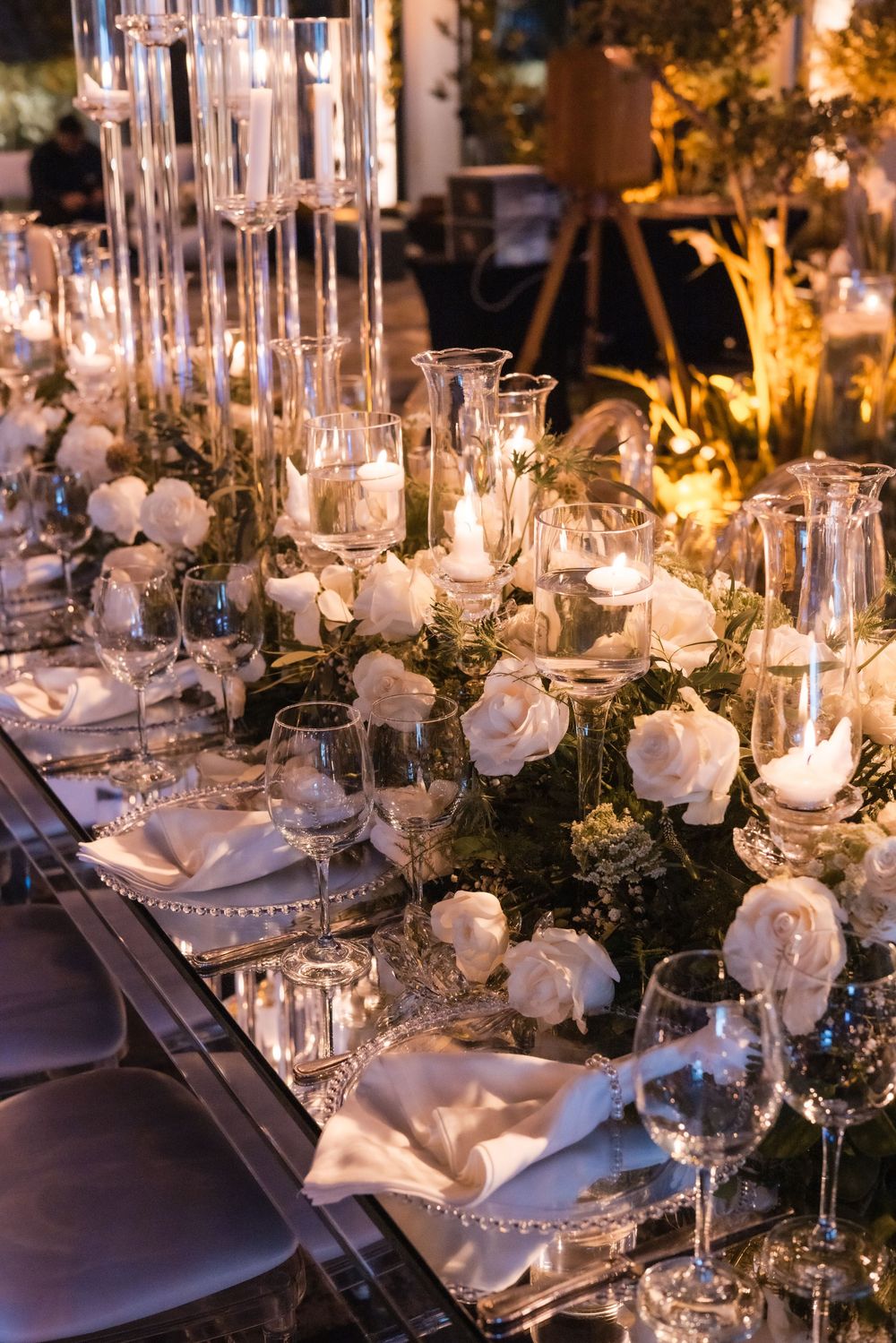 Elegant wedding table setting with white roses, crystal candleholders, and glowing candles creating a romantic atmosphere.