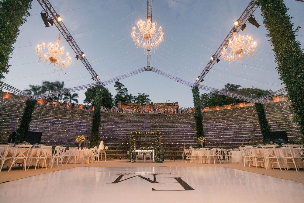 Elegant outdoor wedding venue with crystal chandeliers, white dance floor and amphitheater-style seating at dusk.