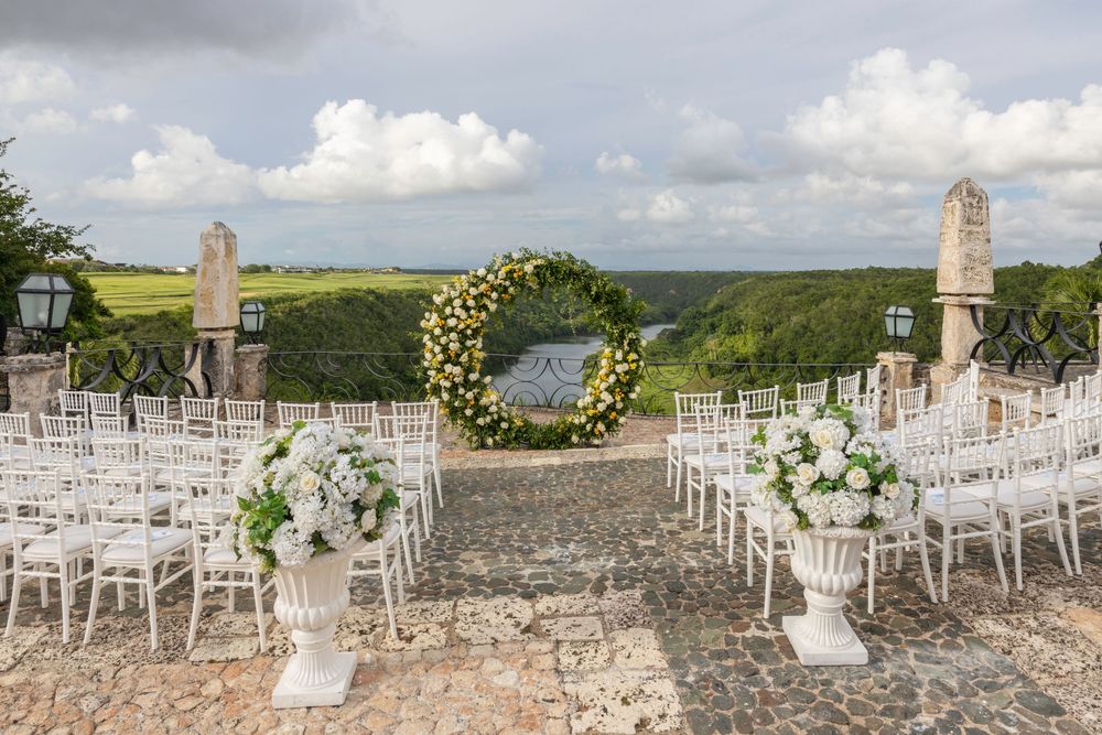 White chairs arranged in rows for an outdoor wedding ceremony with stone walls and ocean views in the background.