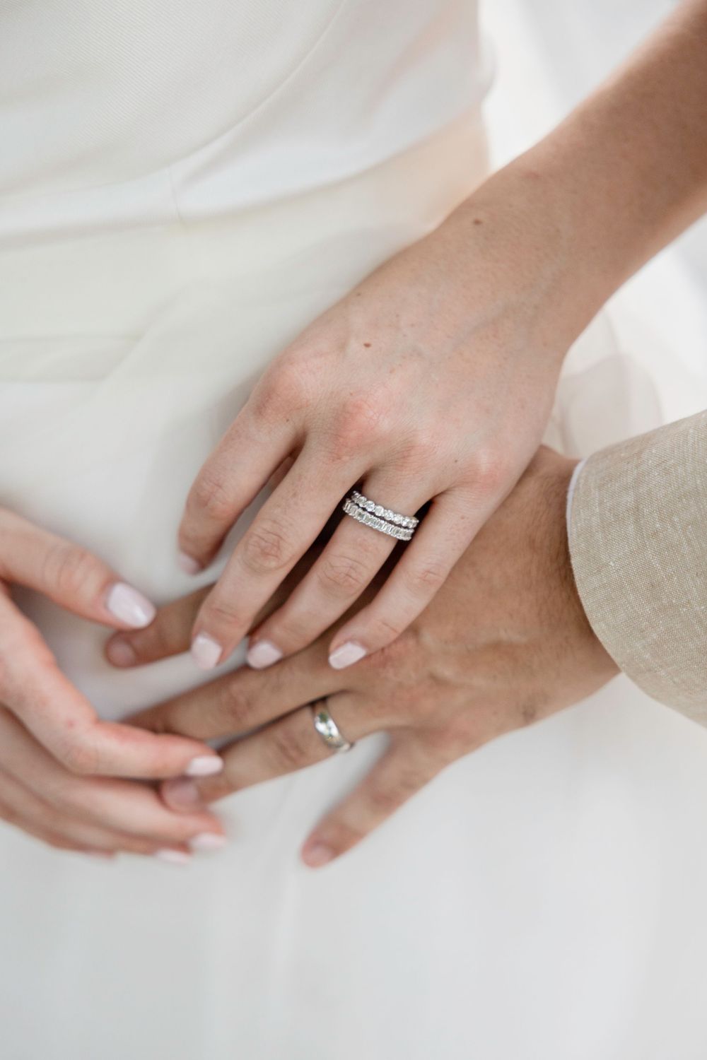 Close up view of hands wearing diamond engagement rings against a white background.