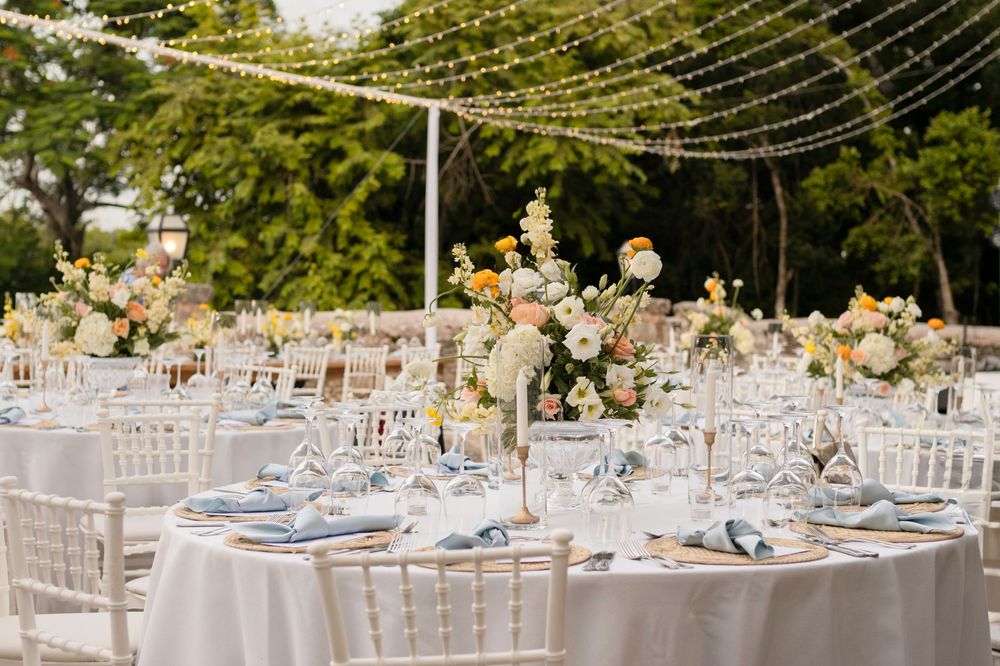 Elegant outdoor wedding reception setup with white tables, floral centerpieces and string lights creating a romantic ambiance.