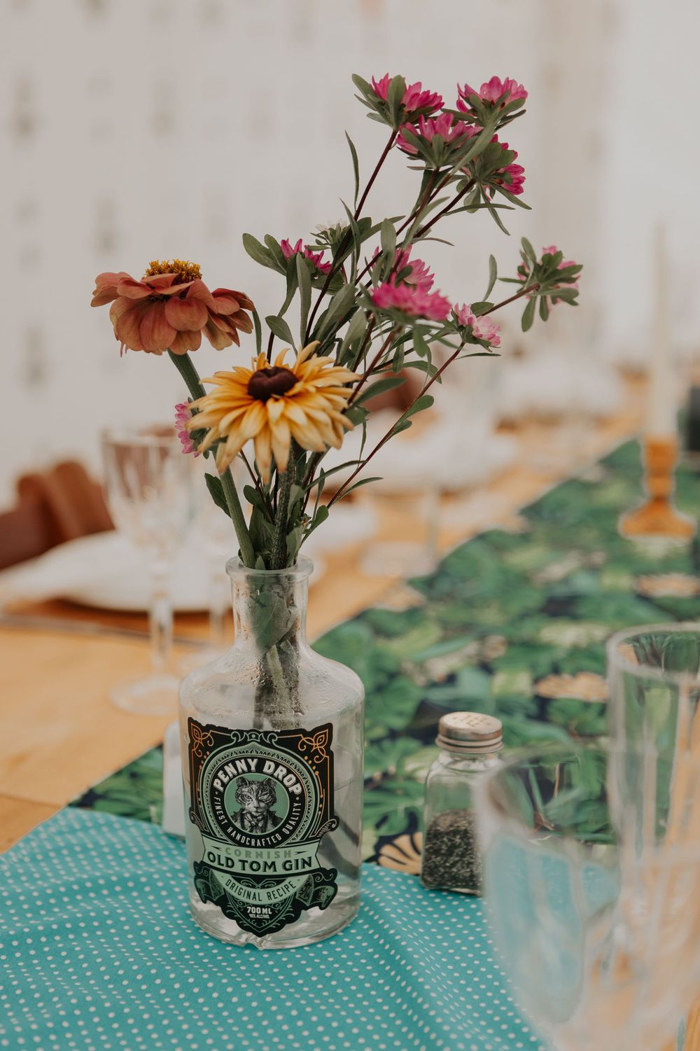 Wildflowers arranged in a Penny Dropt Old Tom Gin bottle centerpiece on a teal floral table runner.