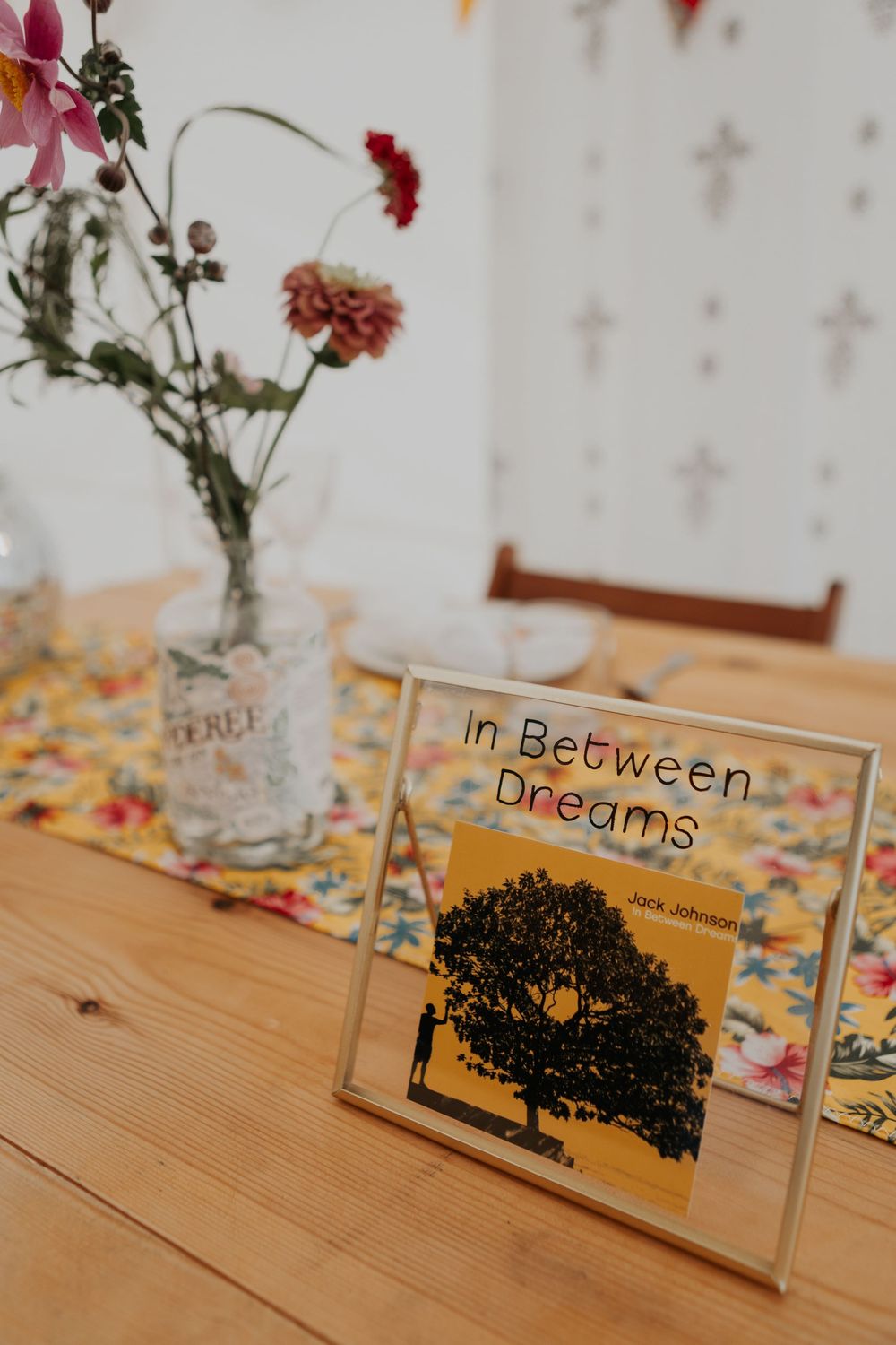 Jack Johnson In Between Dreams album displayed as wedding table name on wooden reception table.
