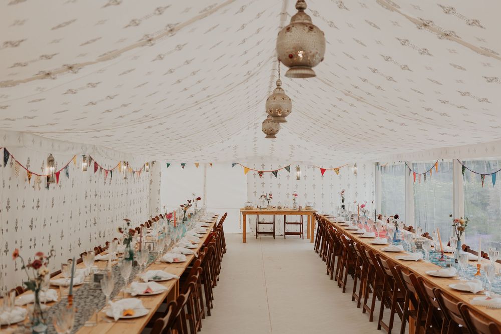 Spacious wedding marquee with two long banquet tables, Moroccan lanterns, colorful bunting, and floral decor.