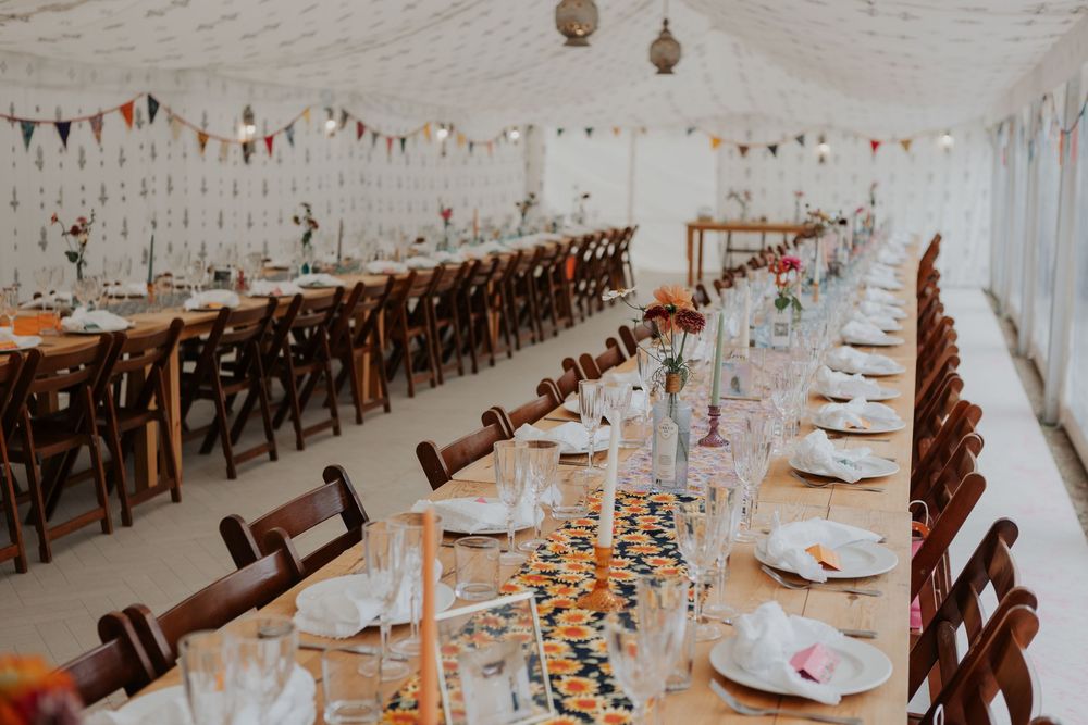 Wedding reception marquee with long tables featuring colorful citrus runners, floral centerpieces, and bunting.