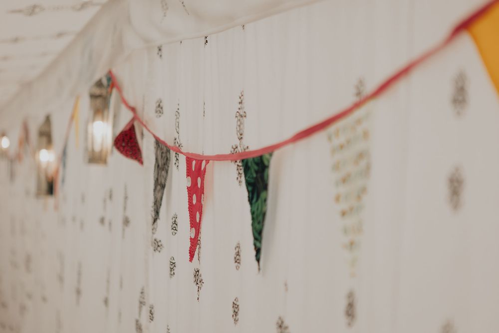 Colorful bunting flags hanging in a decorated wedding marquee with patterned white walls and fairy lights.