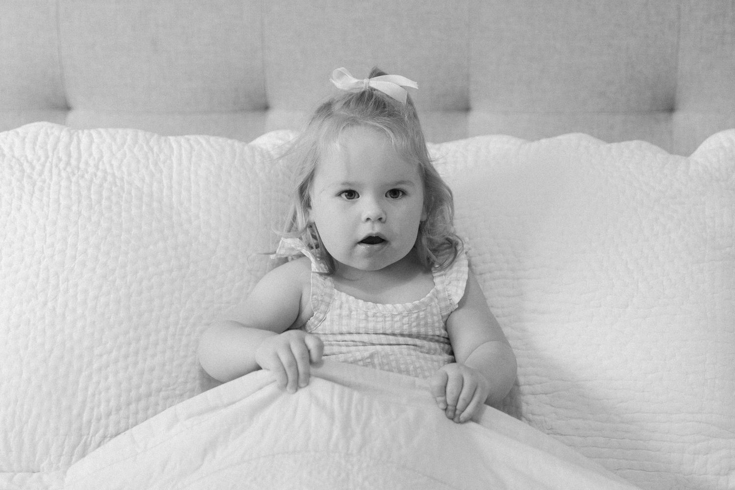 A series of black and white photographs showing a baby lying on white bedding in different poses.