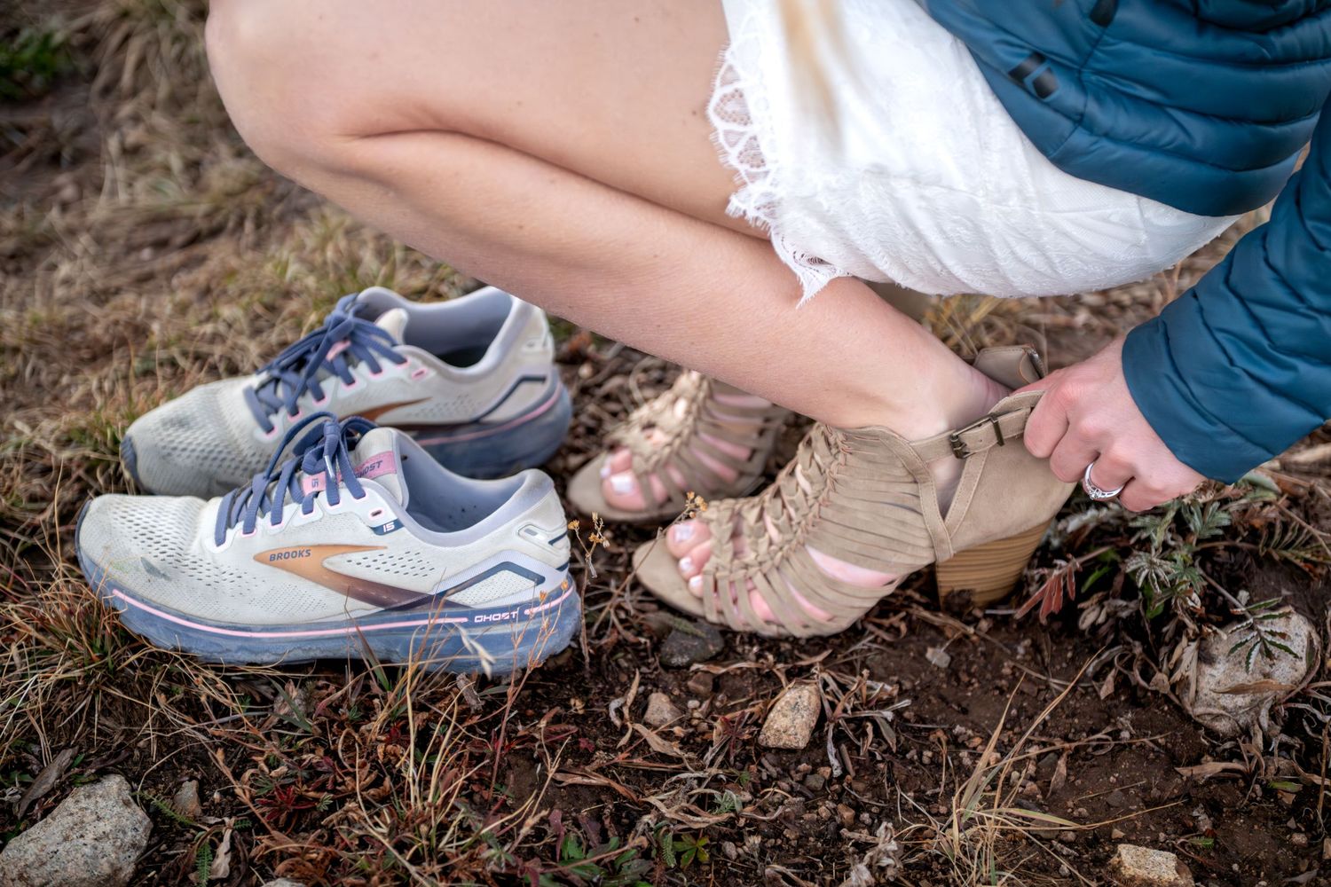 A closeup of bride changing from her high heel shoes back into her tennis shoes. She is squatting down and unzipping the back of her heels.