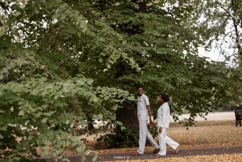 Two people in white attire walk together along a tree-lined path during a romantic outdoor photo session.