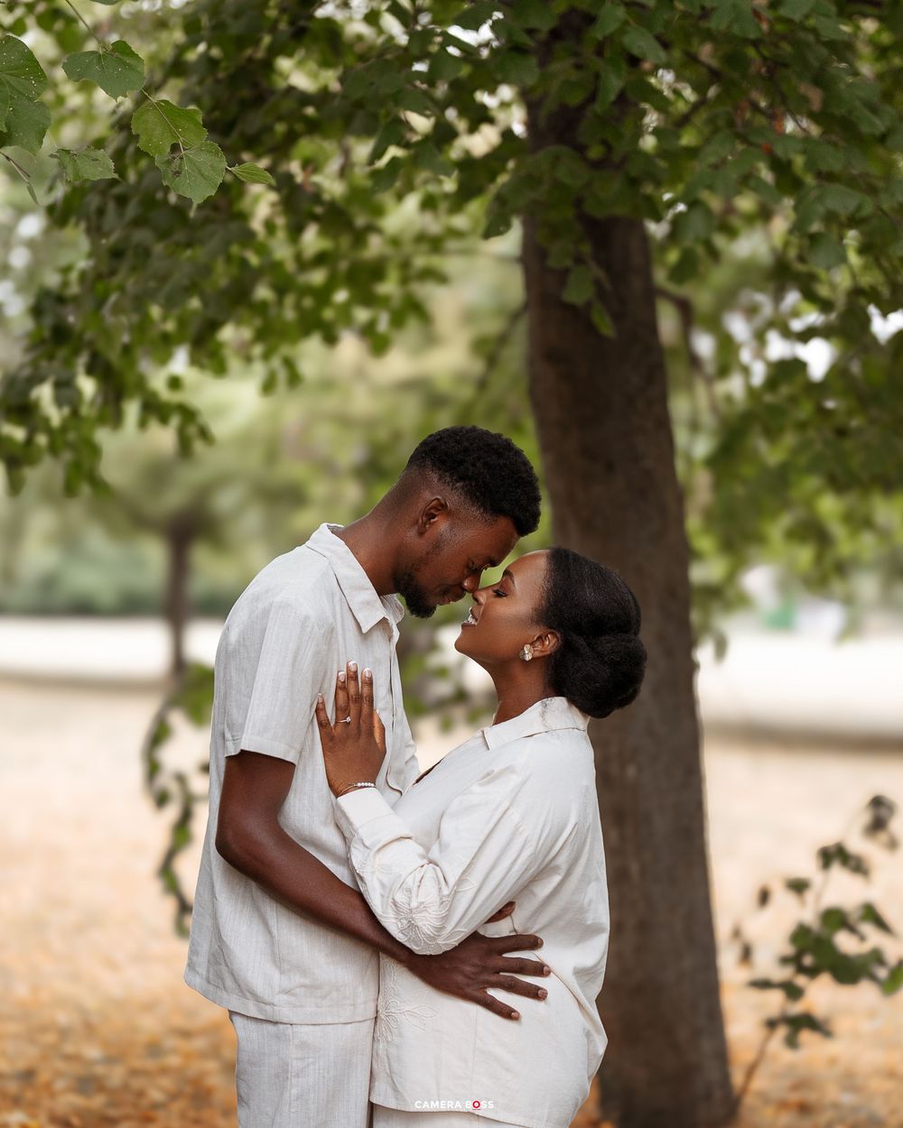 A romantic engagement photoshoot sequence under trees showing a couple in white outfits embracing each other.
